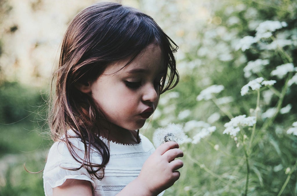 A young girl with brown hair holds a white flower in a sunkissed garden