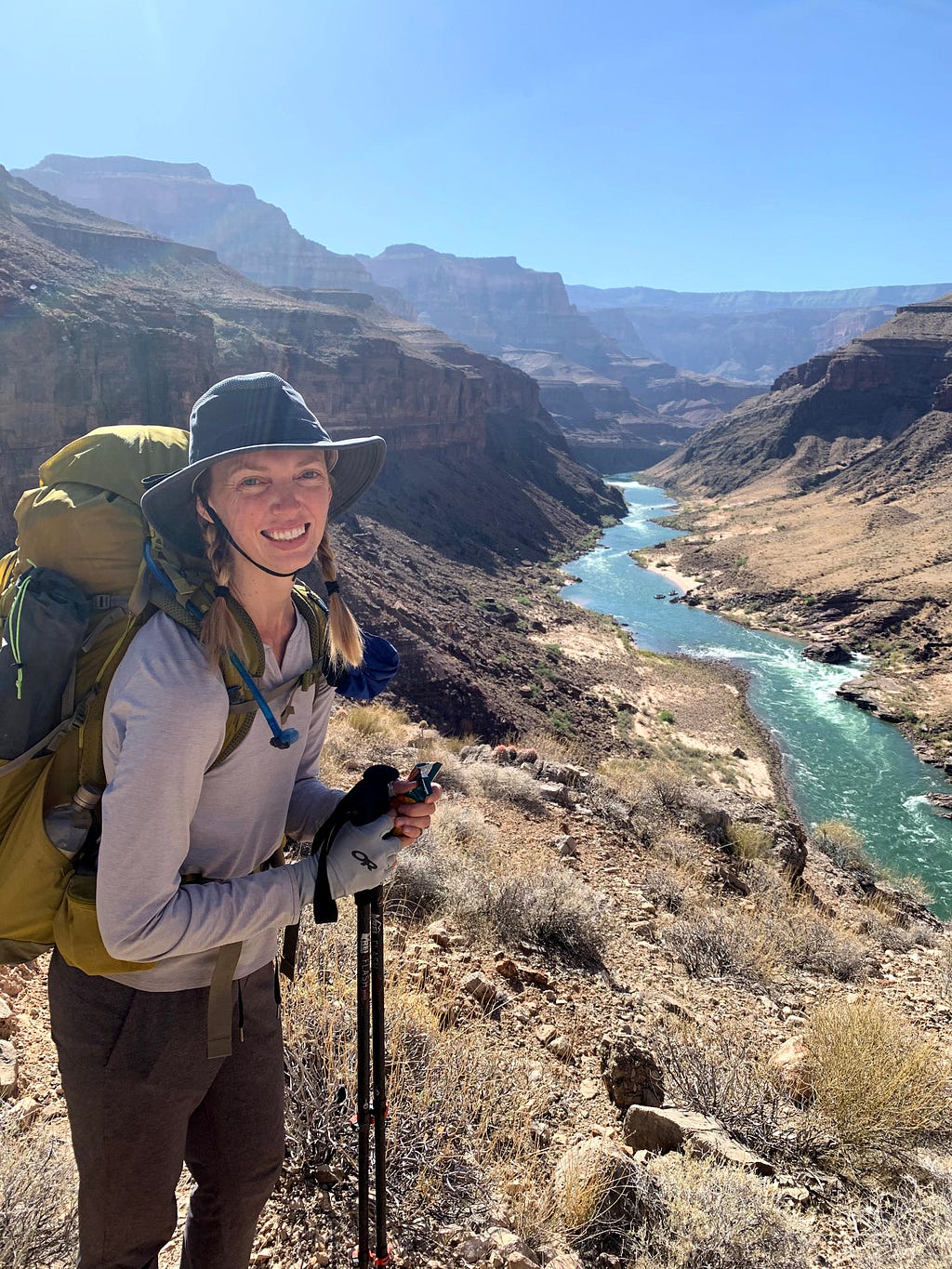 Woman smiling, wearing a backpacking backpack with a view of the Colorado River inside the Grand Canyon
