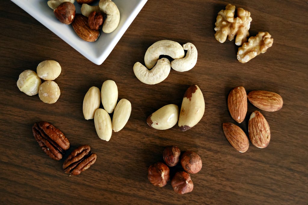 A variety of nuts, separated by each type and placed on a wooden table.