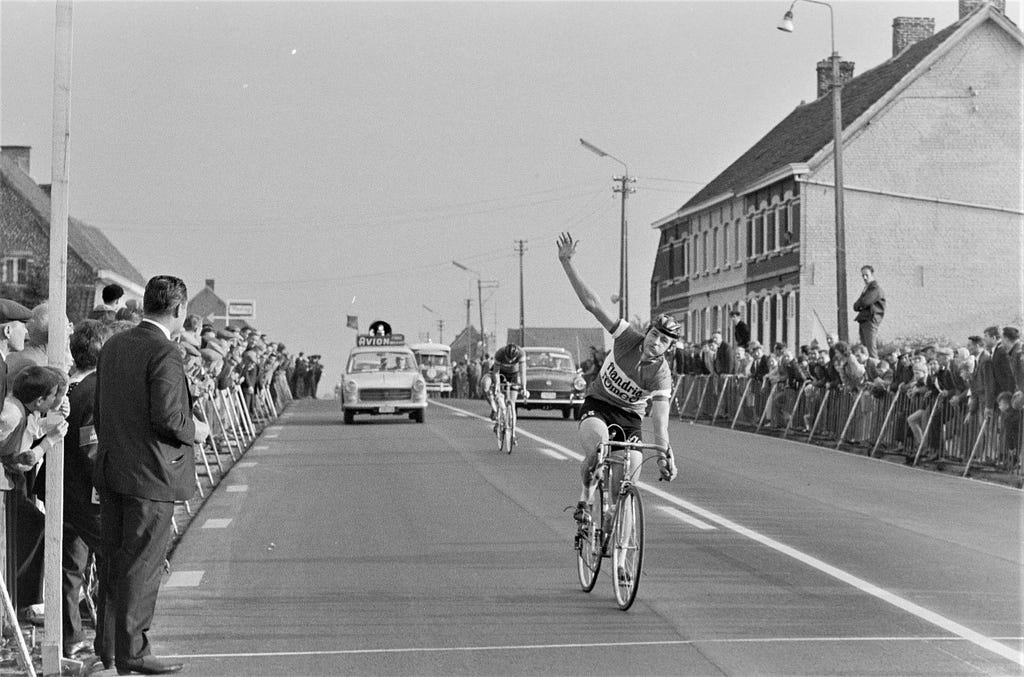 Black and white photo of a cyclist waving to the crowd