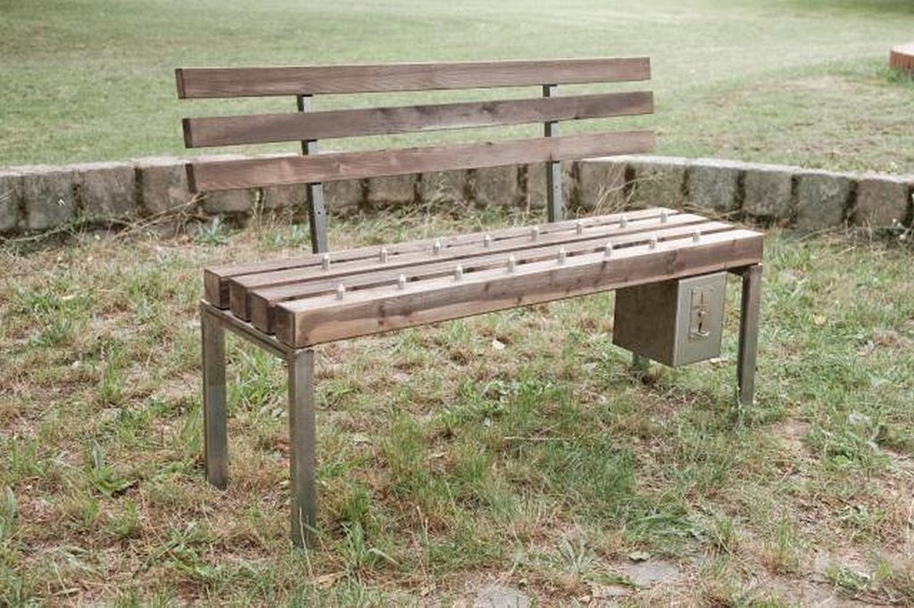 wooden public bench with a coin slot attached to the bottom to be used to retract the spikes from the bench