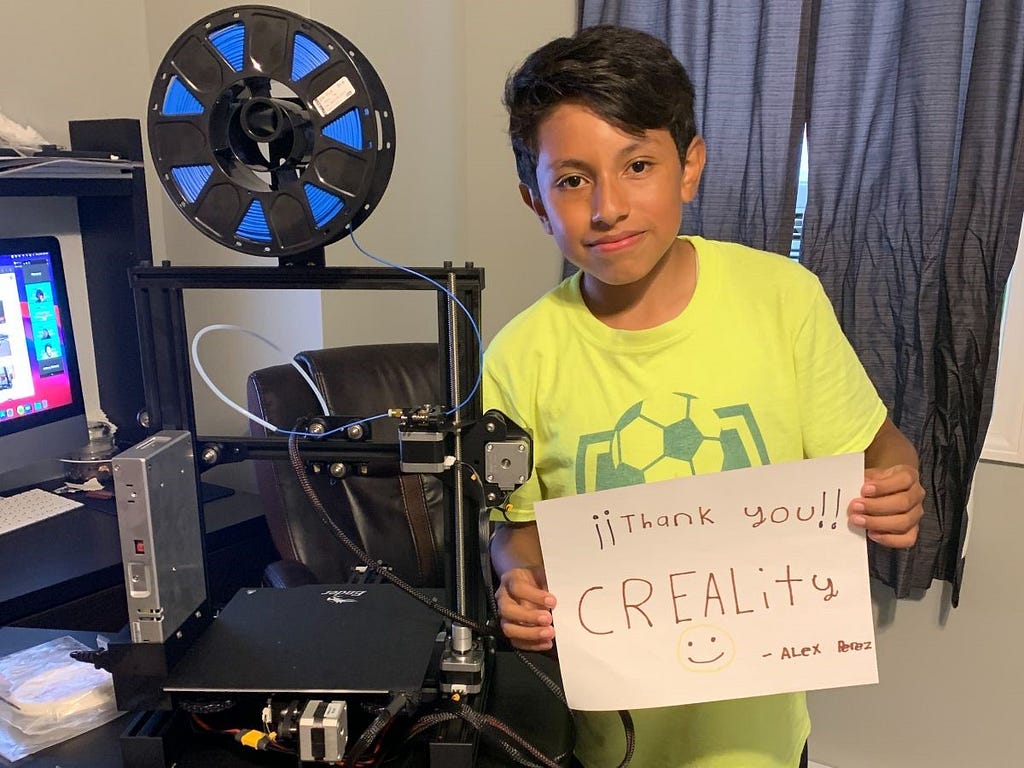 A student standing next to 3D printer holding a written sign that says “¡¡Thank you!! Creality :) -Alex Perez”