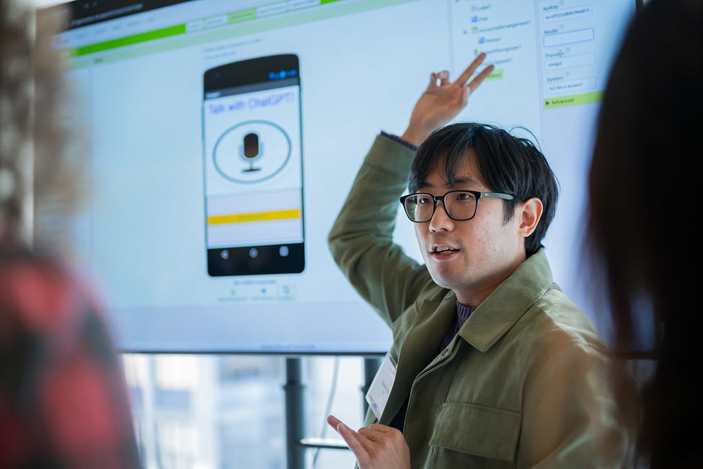 A researcher speaks to people while pointing at a screen.