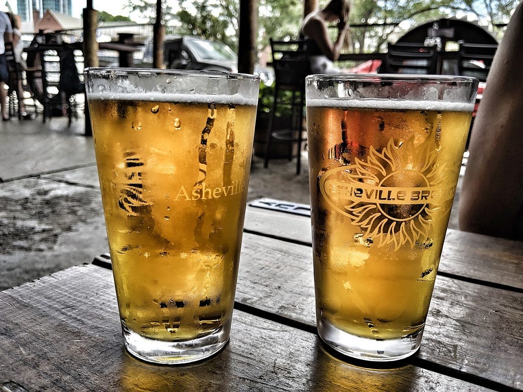 Two pints of pale ale with city street in background.