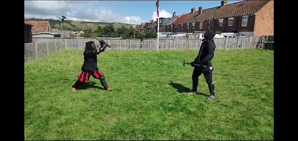 Two men holding halberds facing each other on grass. One of the men is wearing plunderhosen.