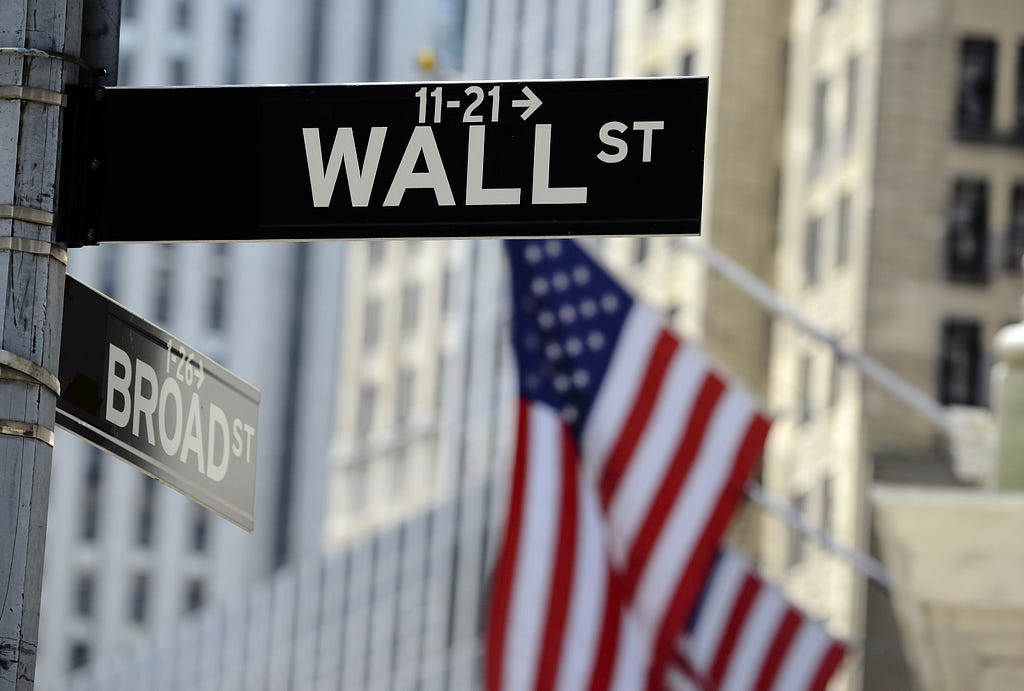 Wall street sign with focus on sign, blurred American flag background