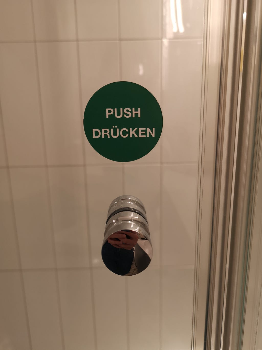 One side of the shower door in the bathroom of the hotel with a push signifier written in a round sticker.