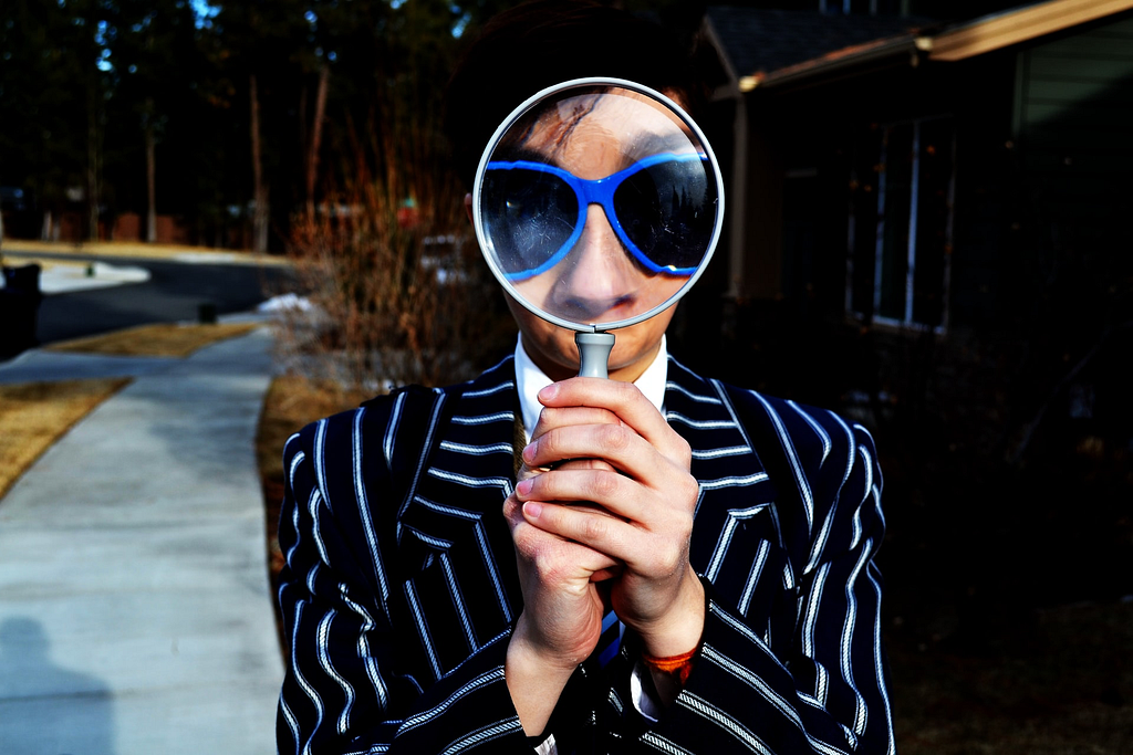 a person wearing a striped suit with a magnifying glass in front of their face magnifying their eyes covered with sunglasses