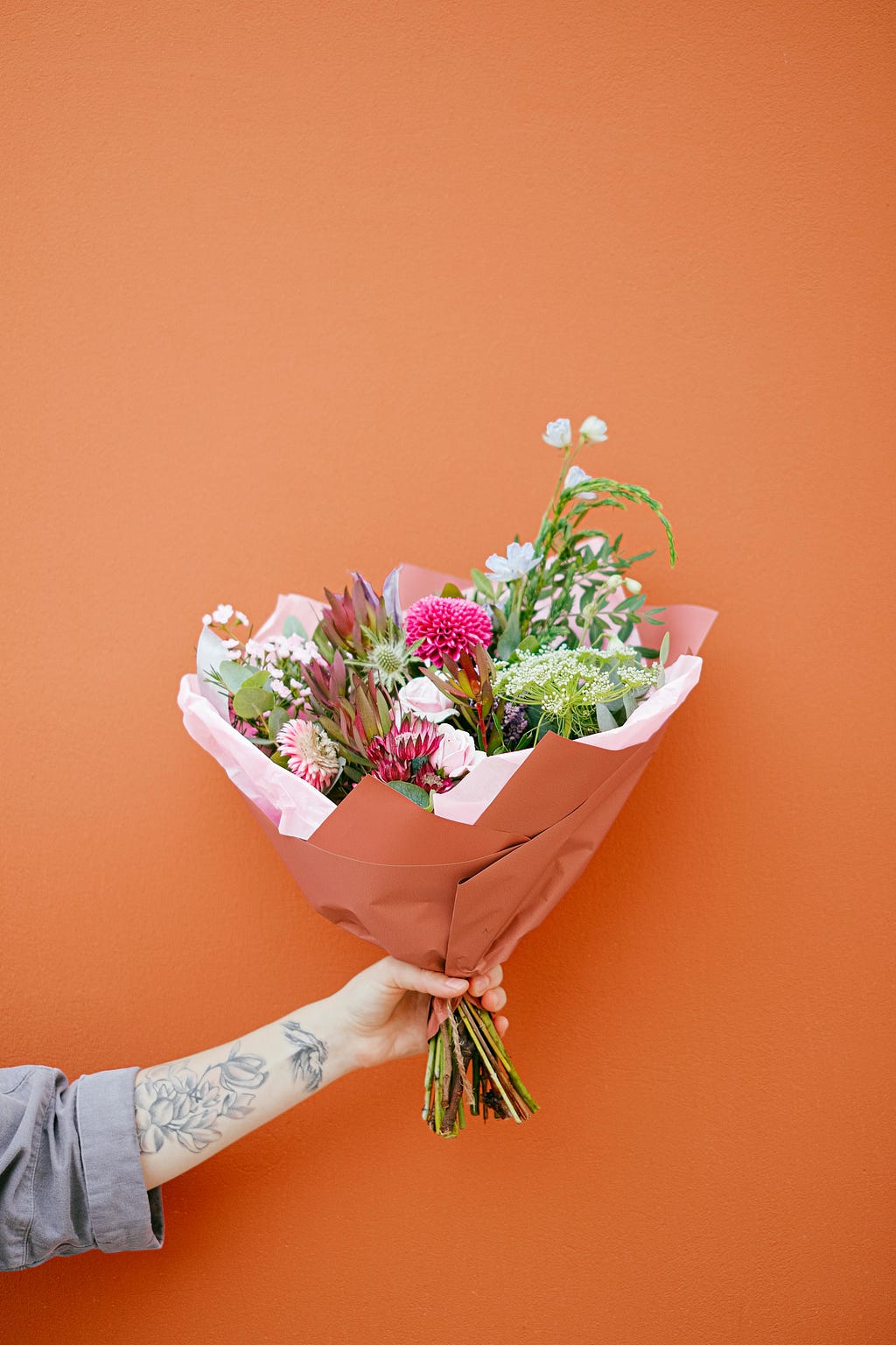 Hand and arm holding a bouquet of flowers on an orange background.