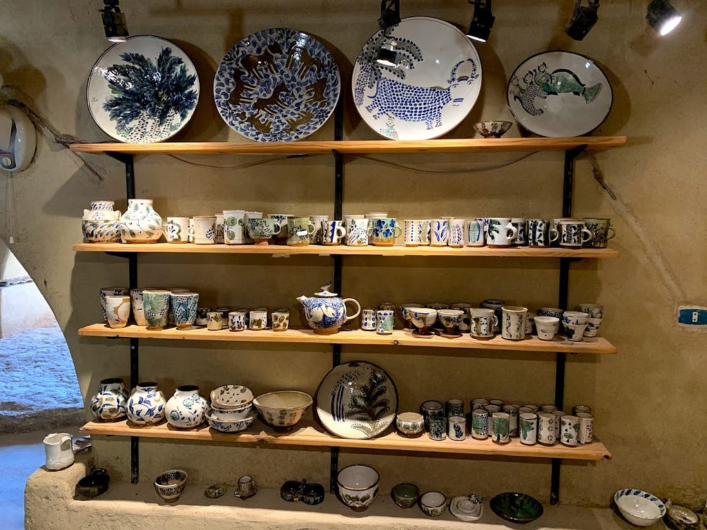 In a rustic boutique, shelves are full of pottery plates, mugs and tea pots