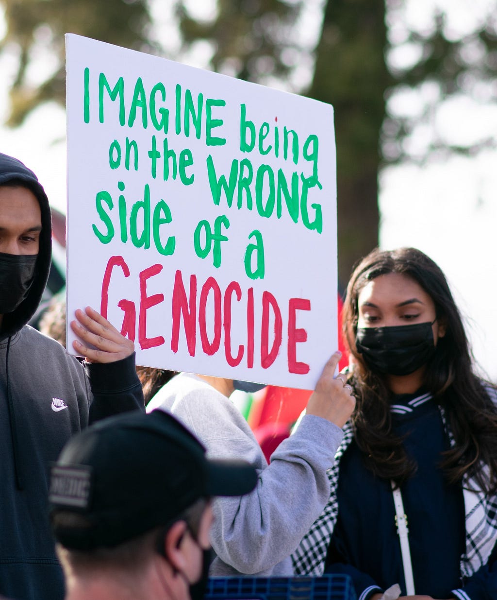 A masked protester holding a sign that says, “Imagine being on the wrong side of genocide.”