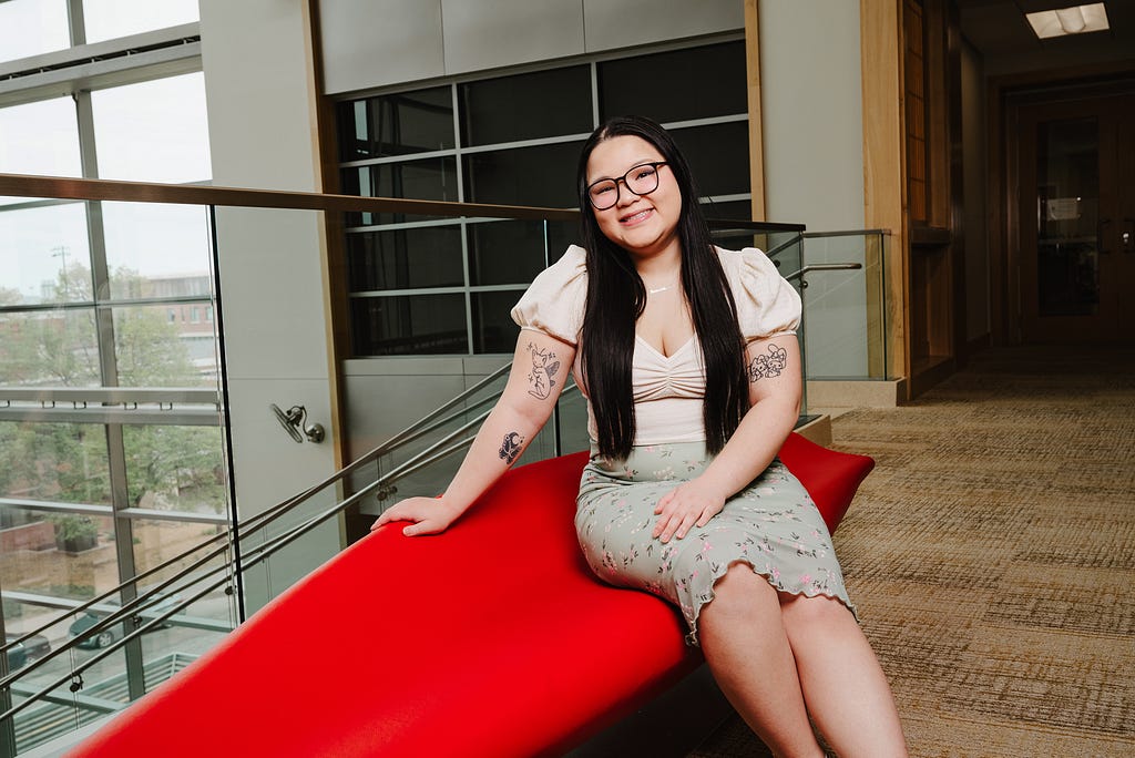 Ann smiles for a photo while sitting on a red bench in Hawks Hall