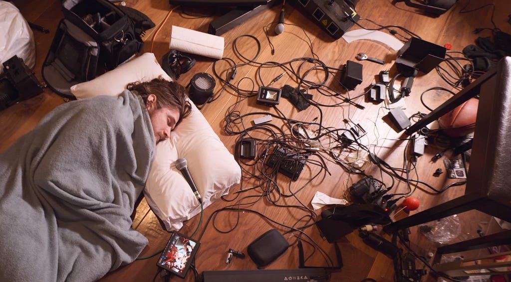 Burnham lies on a pillow on the floor, covered by a blanket and surrounded by wires and electrical equipment.