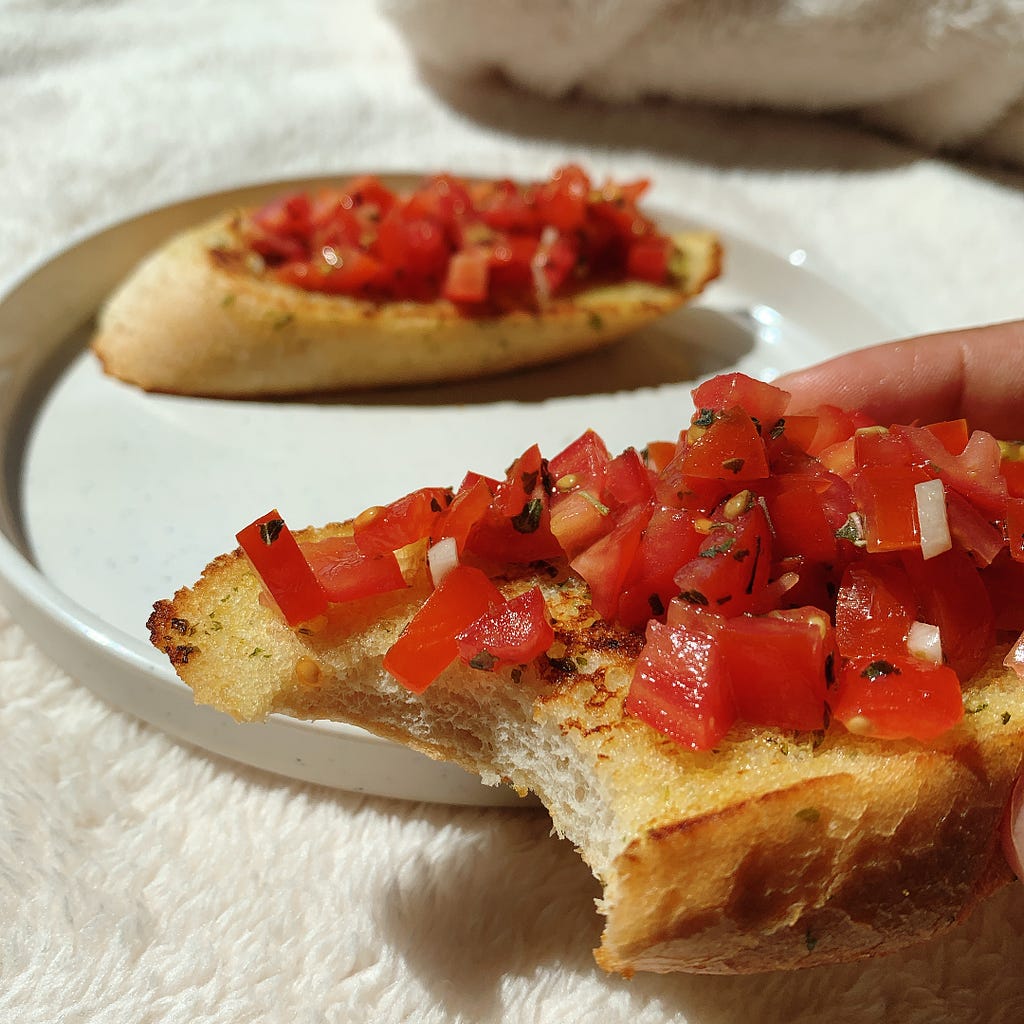 A Delicious Slice of Bruschetta! Simple and Enjoyable! Toasted Garlic Bread topped with Tomatoes, Garlic, Fresh Herbs, Olive oil! A super easy & delicious recipe!