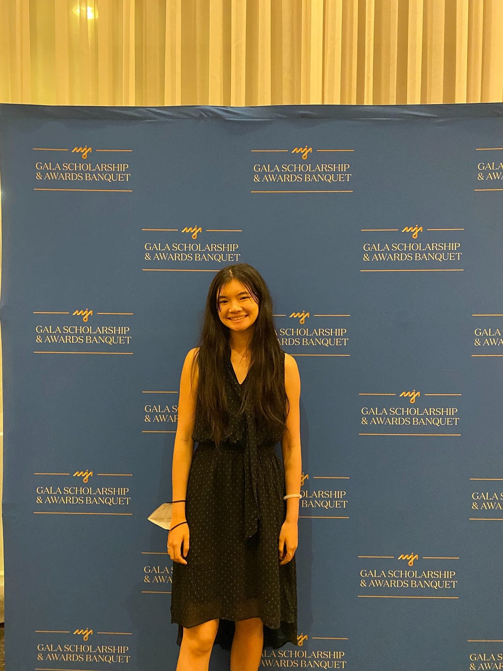 woman wearing black dress standing in front of background that says AAJA Gala Scholarship and Awards Banquet