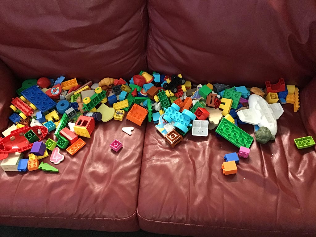 a red sofa with a lot of duplo blocks of various colours piled on it.