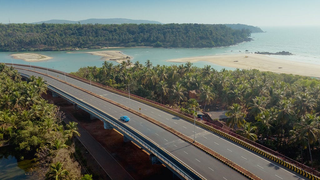 Skoda Slavia driving on a scenic highway in Goa, surrounded by lush green trees on both sides