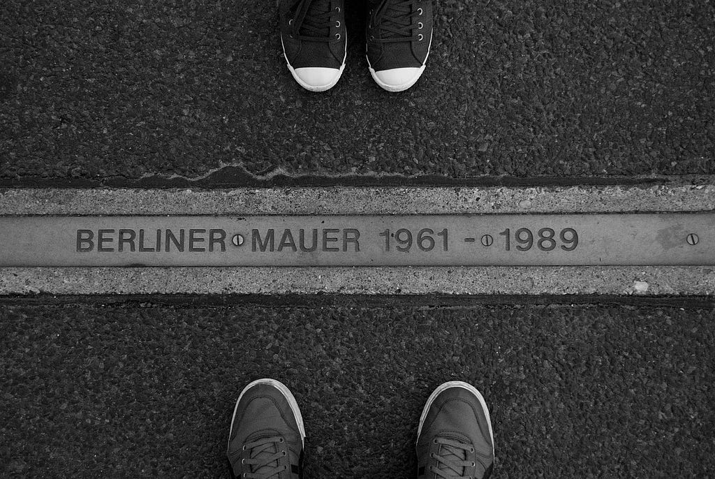Remains of the berlin wall, flat plaque in the ground with pairs of feet on each side, open source from Pixabay Abian_Valido