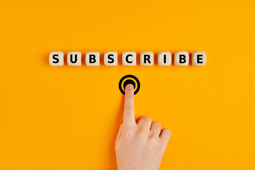 Photo of the word “Subscribe” on dice and a person’s hand pressing a drawn button