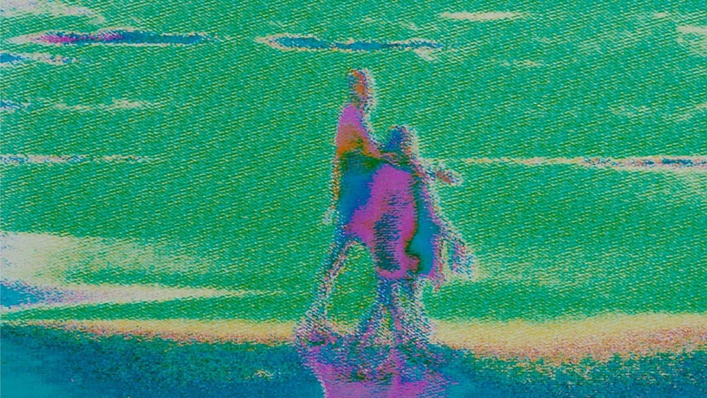 Movie still showing two figures walking near a sea shore. The colours are green and lavender and the image is full of static and distortions.