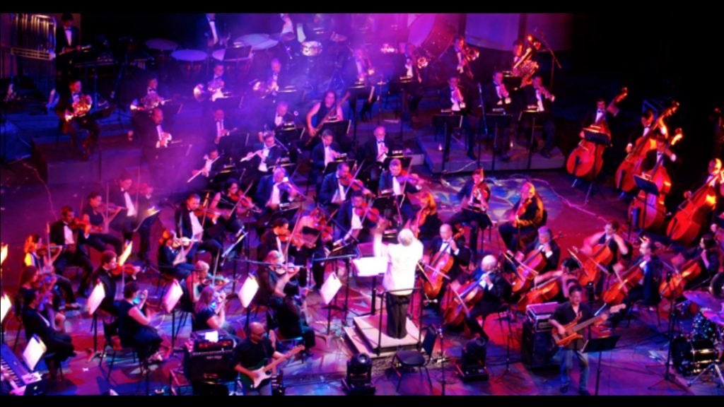 An orchestra being conducted by man in a white jacket