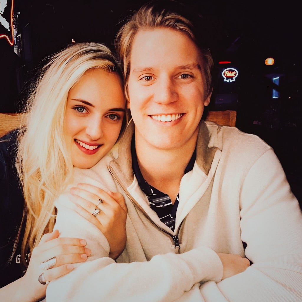 Smiling couple posing together at a lively bar with drinks in hand and dim ambient lighting