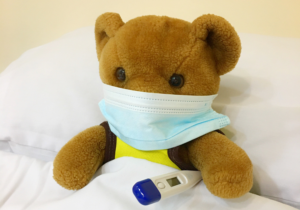 Bamse i hospitalseng med termometer og munnbind.