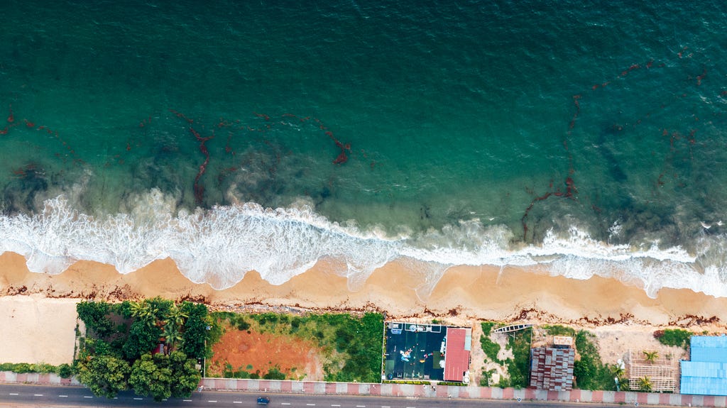 Foto aérea de uma praia com casas na orla e o mar ao fundo