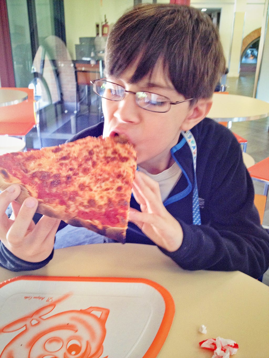 Young boy with glasses eating a large slice of pizza