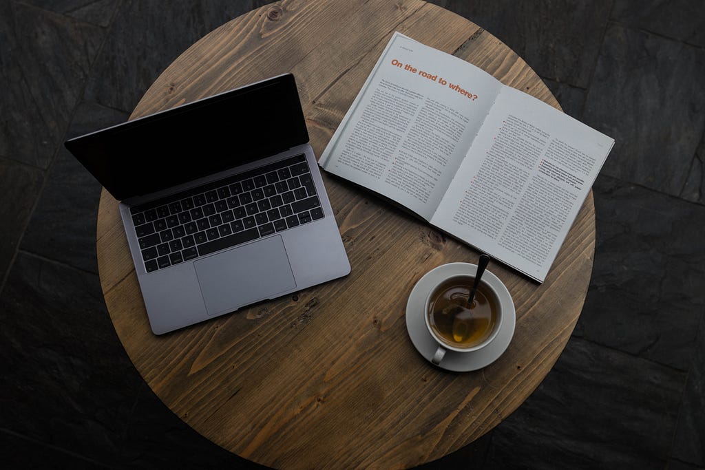 Laptop, open book, and a late on a round wooden table.