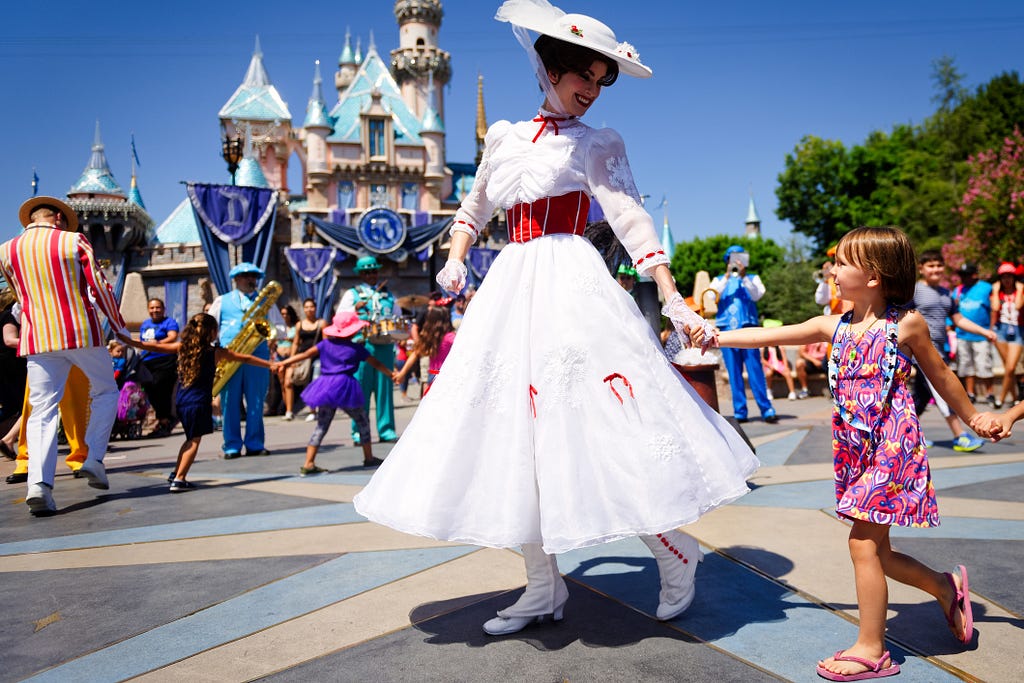 Mary Poppins smiles and leads young children past Sleeping Beauty Castle