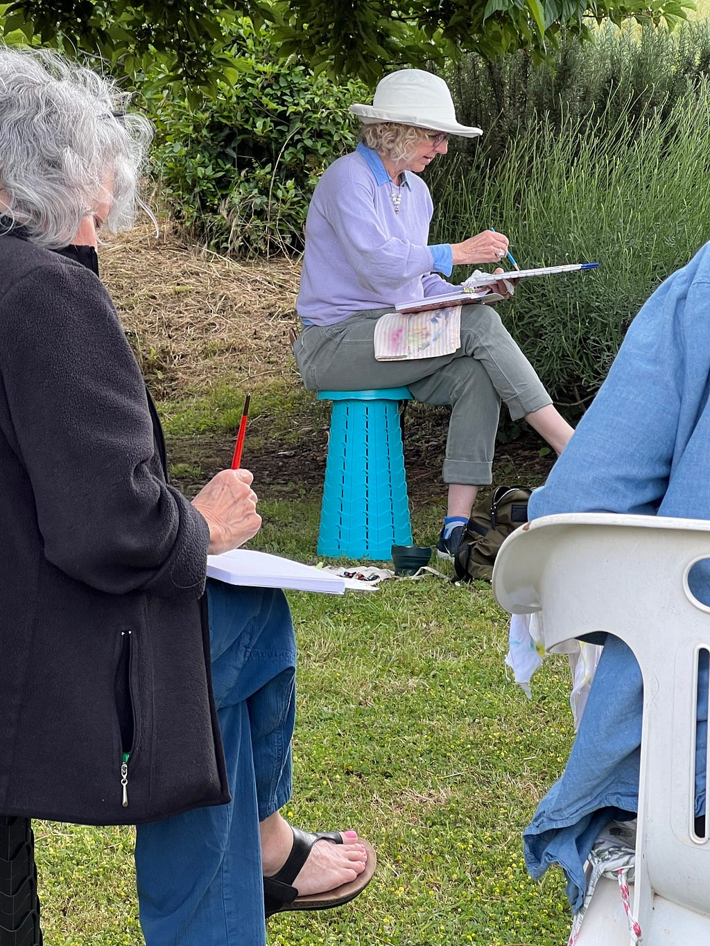 Photo of artist Roxanne Steed in her outdoor painter’s position; sitting with one leg crossed over the other allows grativy to do some work with wet pigment that has a nice effect.