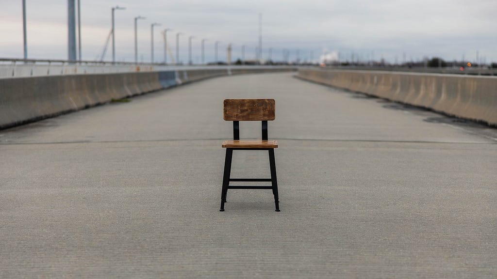An empty chair in the middle of a deserted highway.