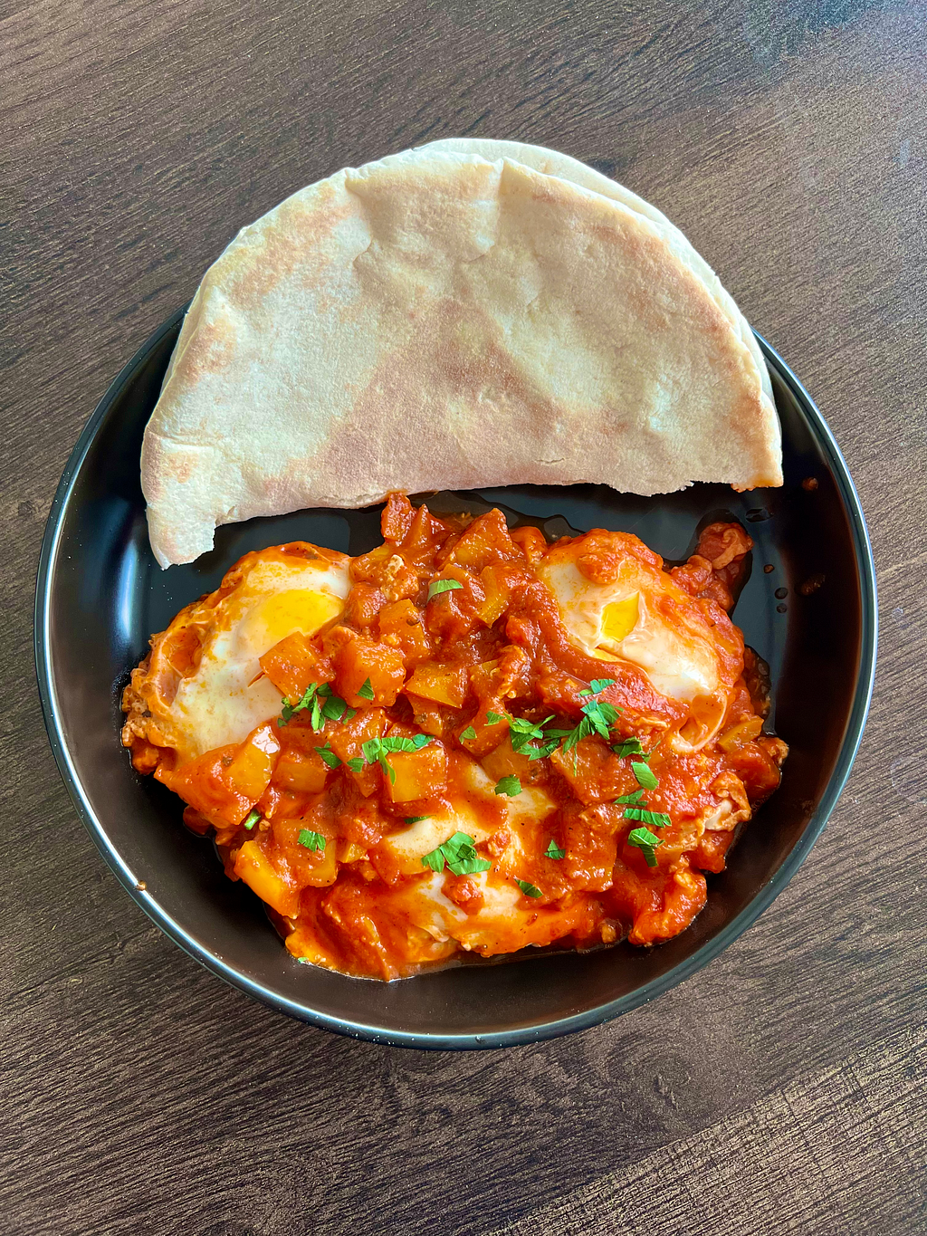 Shakshuka dish pictured on a table with pita bread