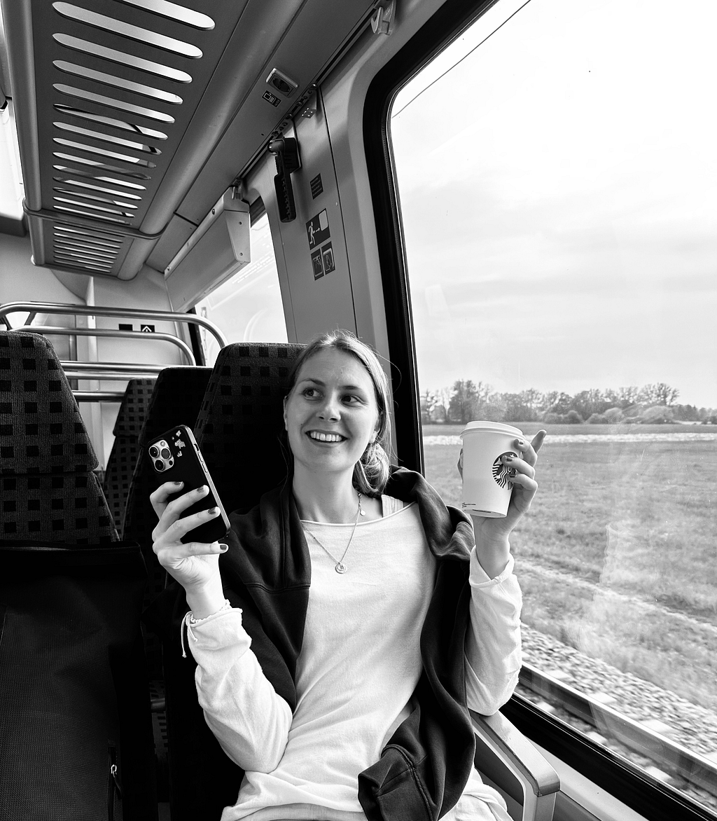 woman smiling sitting on the train holding a coffee cup and phone in the other hand