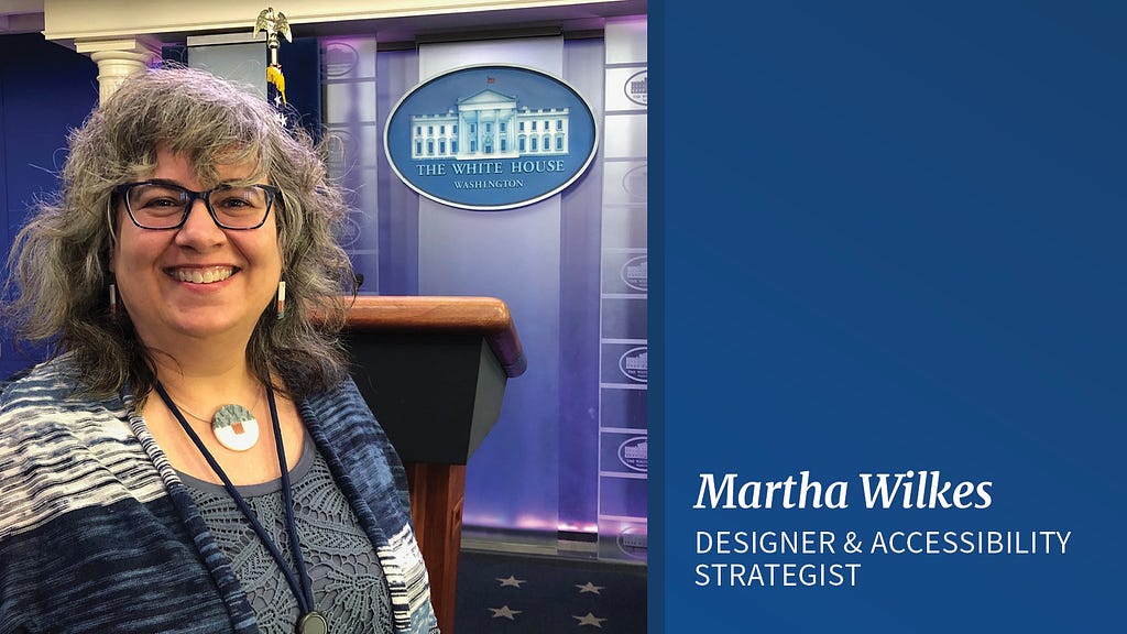 A woman stands in front of a wooden podium and the seal of The White House. She has shoulder-length grey and black hair and wears black glasses. There is a vertical blue line and to the right of that line is white text on a blue background that reads “Martha Wilkes, designer & accessibility strategist”