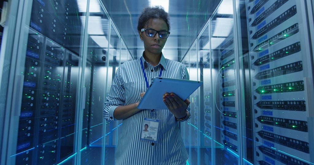 person with a tablet walking through a row of servers