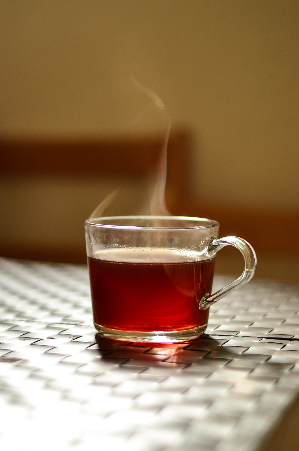 A hot cup of tea in a glass mug with steam rising