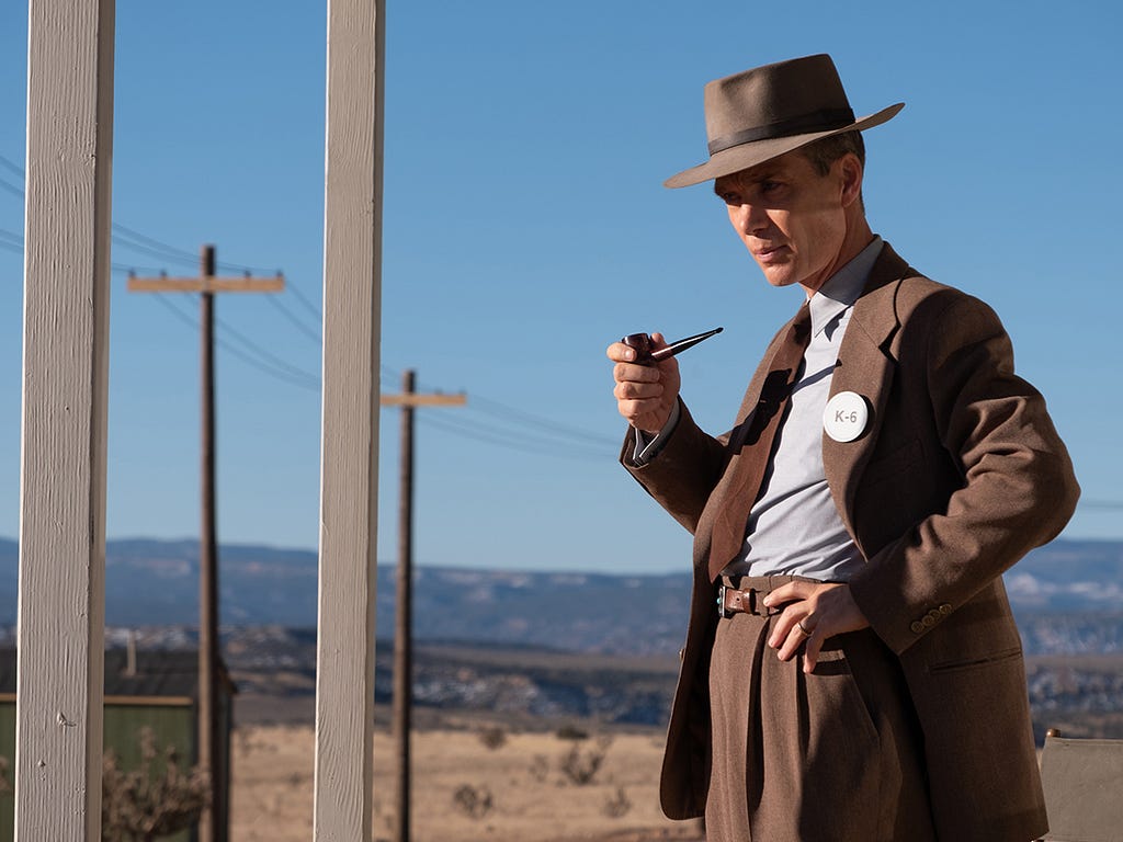 Cillian Murphy as Robert J Oppenheimer. He is standing at the Los Alamos test site holding a smoking pipe in his hand