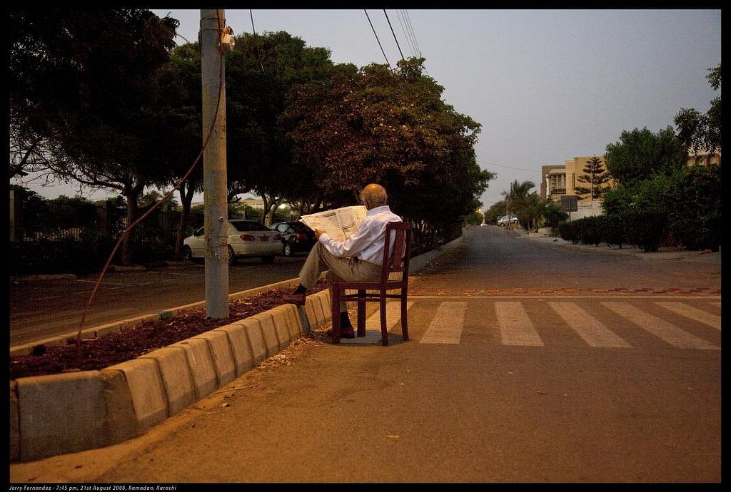 photo of a man sitting on a chair in the street reading a newspaper