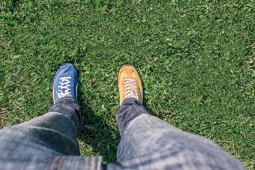 Person wearing mismatched running shoes (one blue, one yellow), standing on green grass.