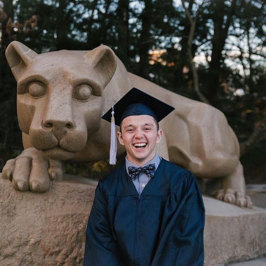 A man standing in front of the Penn State mascot wearing a graduation cap and gown.