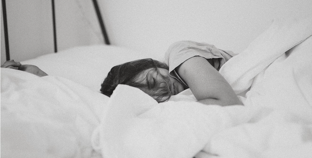 A black and white photo of a woman lying in bed, looking sick and exhausted.