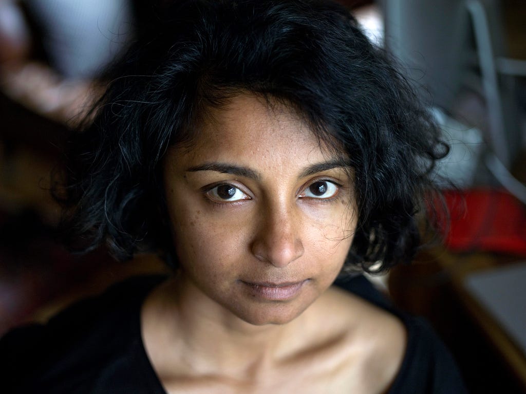 Headshot of author Devika Ponnambalam, with dark wavy hair and black blouse looking at the camera, credit Graham Clark