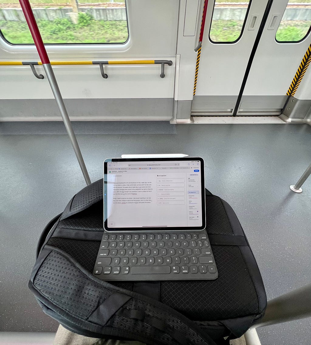 An iPad on top of a backpack on the laps of a person sitting at MTR, Hong Kong. View in the windows: grass and concreet blocks.