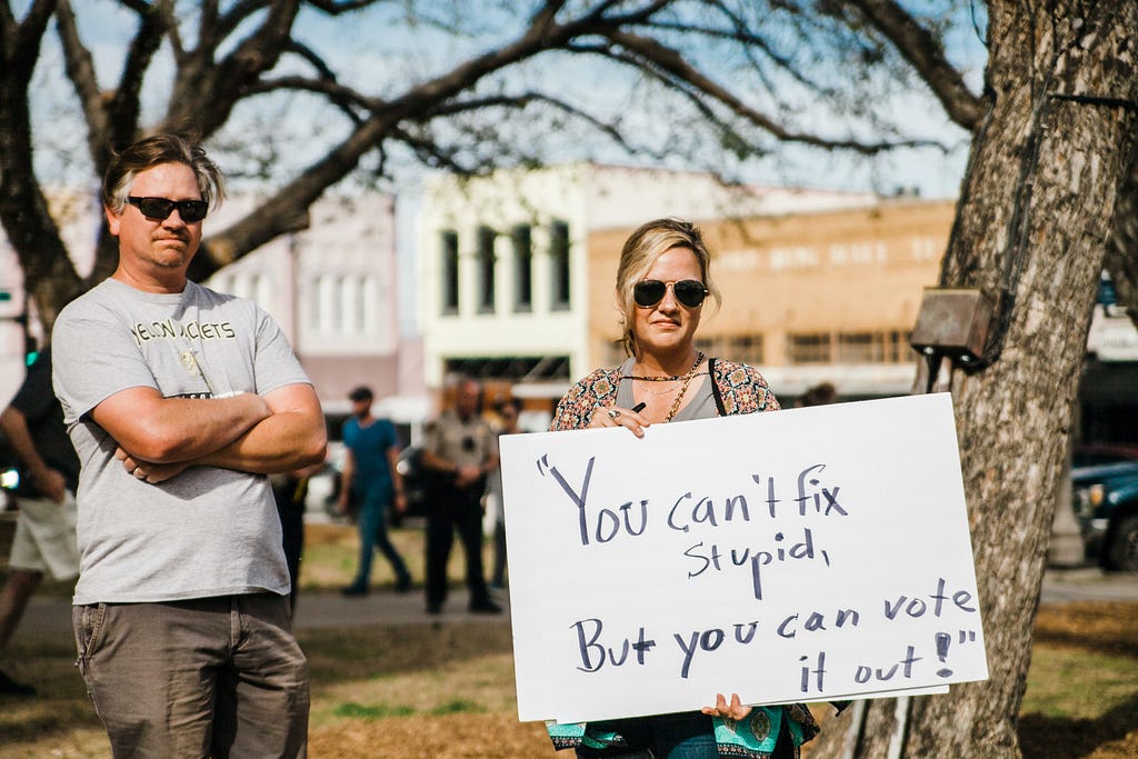 A woman holds a sign reading “You can’t fix stupid, But you can vote it out!”