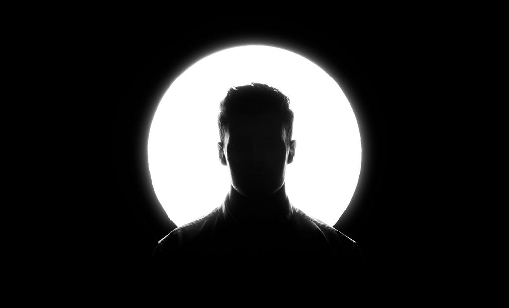 A man’s silhouette in front of a white circle. The photo is in black and white