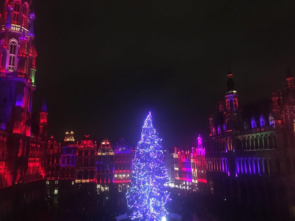 A lit Christmas Tree in the middle of a colourfully lit city square.