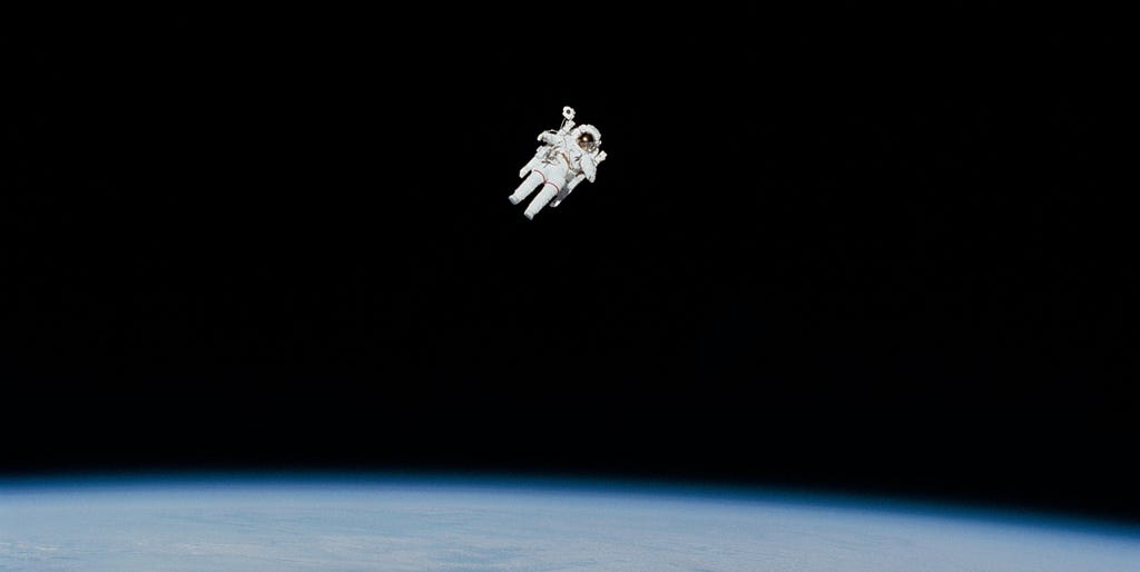 Astronaut EVA above Earth. The astronaut appears to be alone in the deep black of space, and only the implicit existence of the photographer suggests otherwise.