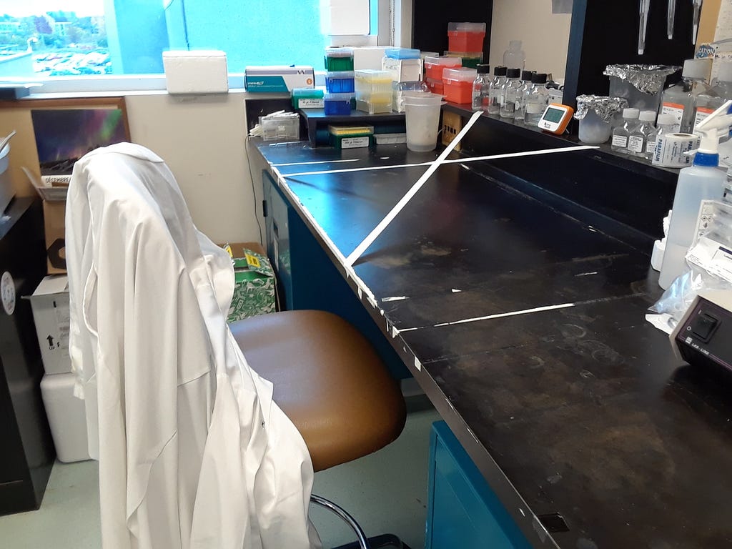 A lab coat over a chair at a university lab station crossed off by tape.